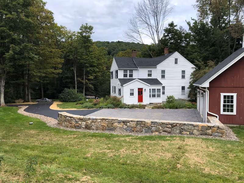 Completed raised paver courtyard beside a red garage, with a stone retaining wall along the lawn.