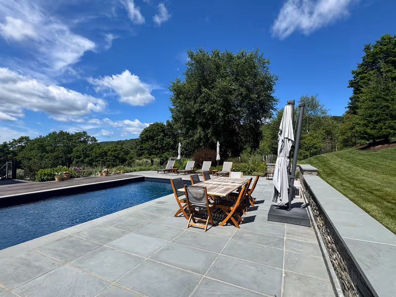 Finished stone pool terrace with dining furniture and surrounding lawn.