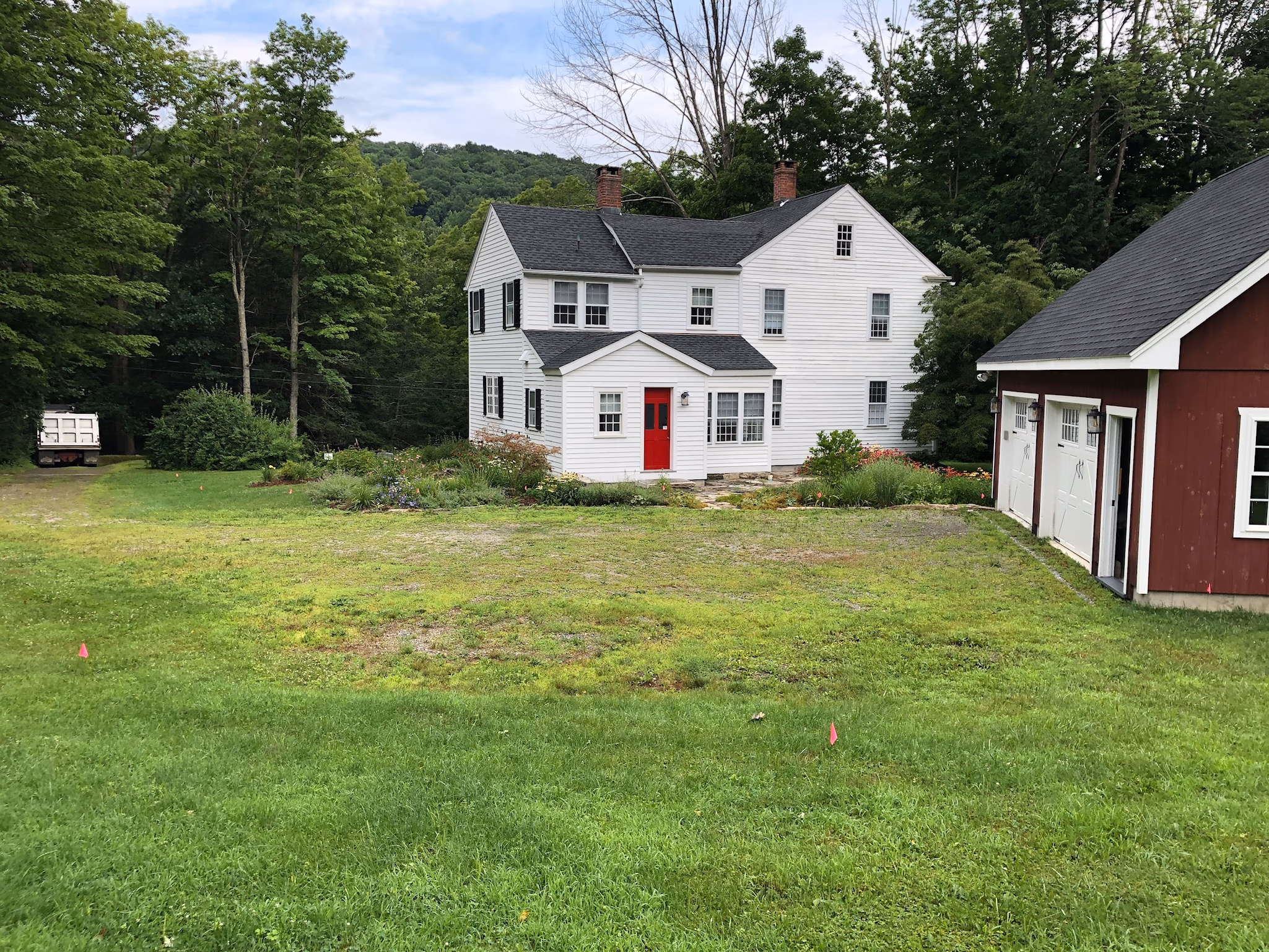 Grass and uneven ground between a white house and red garage before courtyard construction.