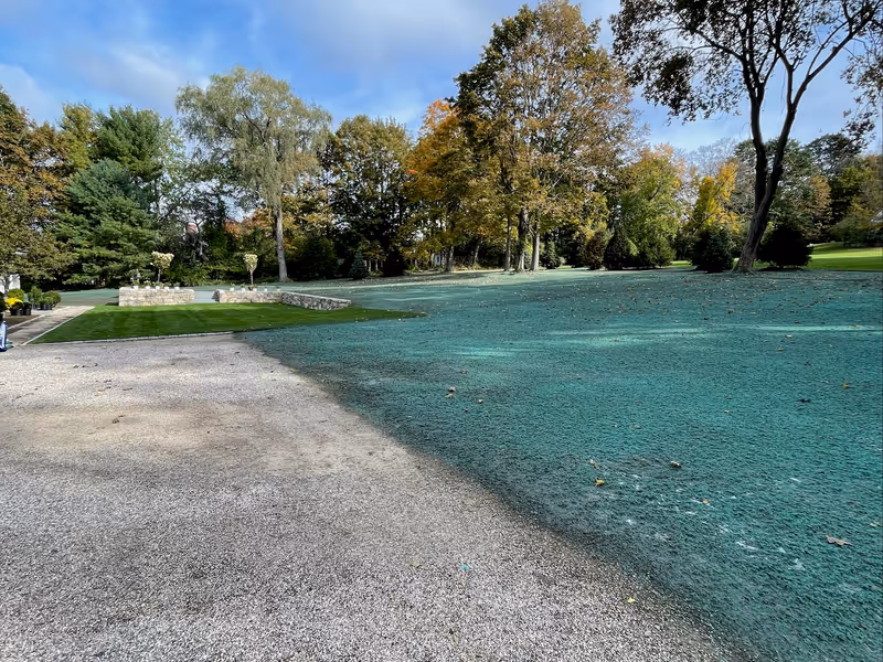 Fresh hydroseeding across graded grounds beside a sod lawn and stone walls.