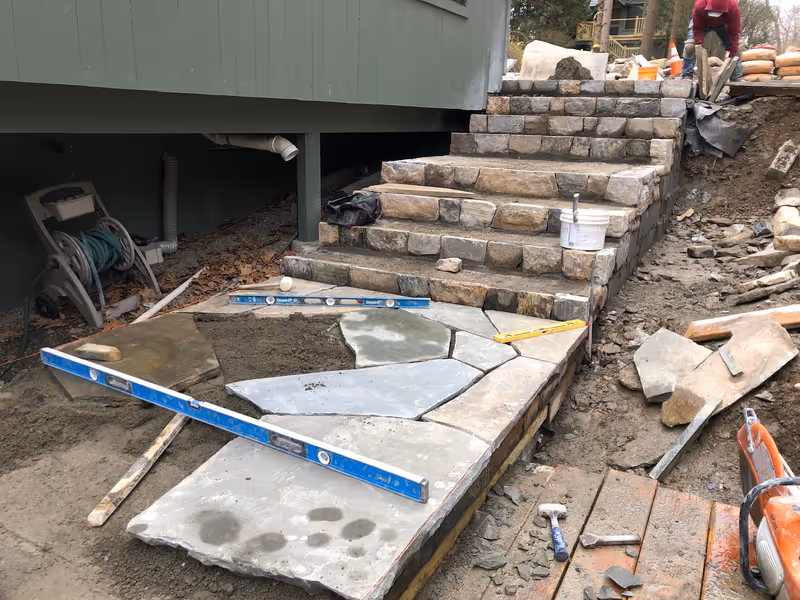 Stone steps and flagstone landing under construction with levels and masonry tools.