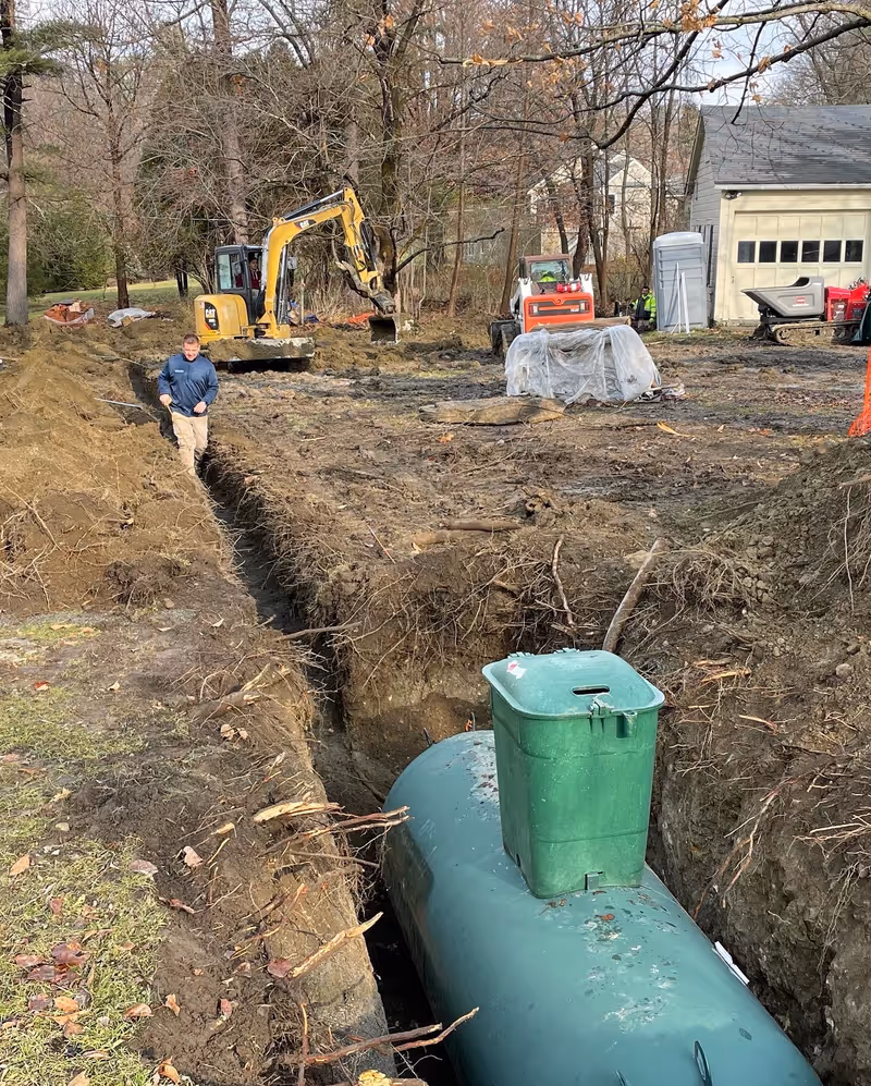 Underground tank in an excavation with a connecting trench and earthmoving equipment beyond.