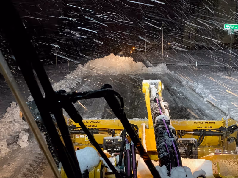 Snow plow clearing a commercial property during winter storm conditions.