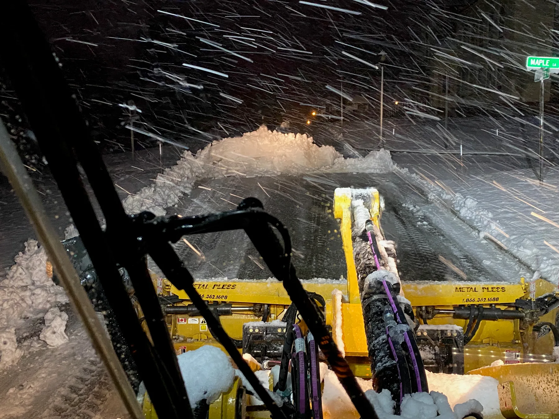 Snow plow clearing a commercial property during winter storm conditions.