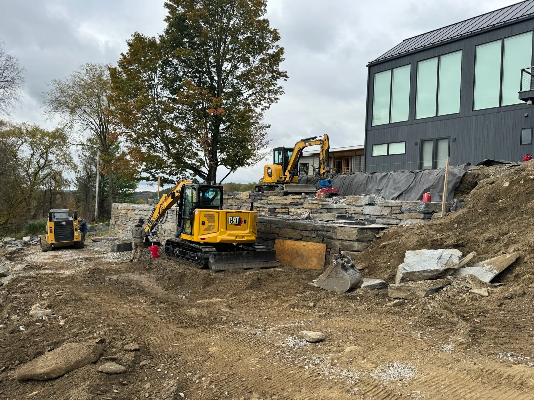 Tiered stone wall construction with excavation equipment at a residential property.